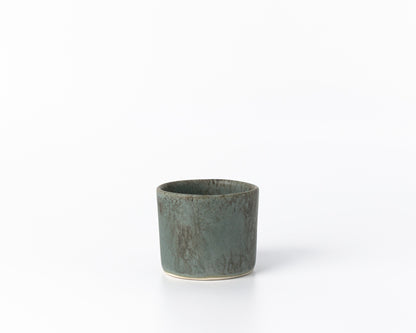 Small green ceramic cup with speckled matte finish on white background