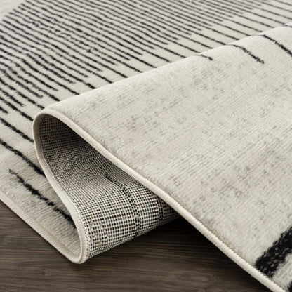 Close-up of Angus abstract black and white area rug, showing striped pattern, curled edge, and backing on wood floor.