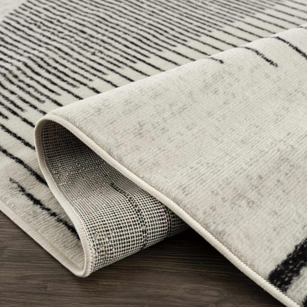 Close-up of Angus abstract black and white area rug, showing striped pattern, curled edge, and backing on wood floor.