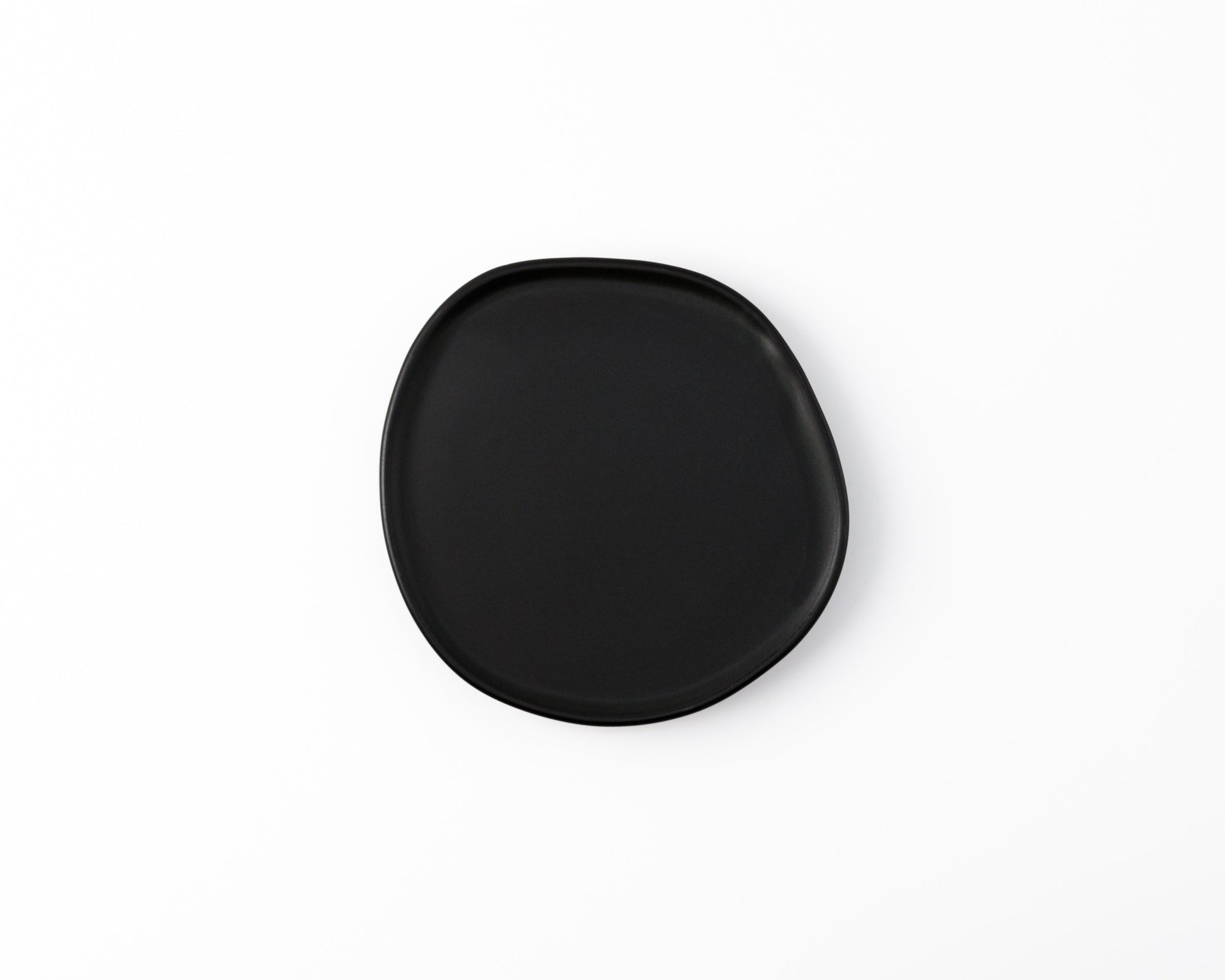 Minimalist black ceramic plate with irregular shape on white background