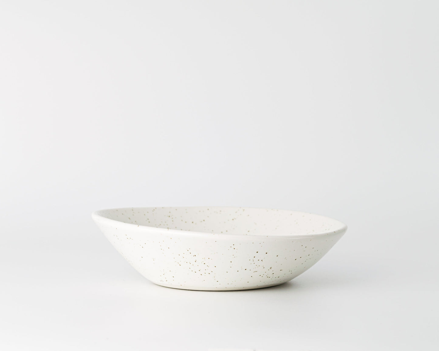 Minimalist white ceramic soup bowl with brown speckled pattern on plain background
