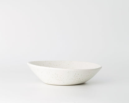 Minimalist white ceramic soup bowl with brown speckled pattern on plain background