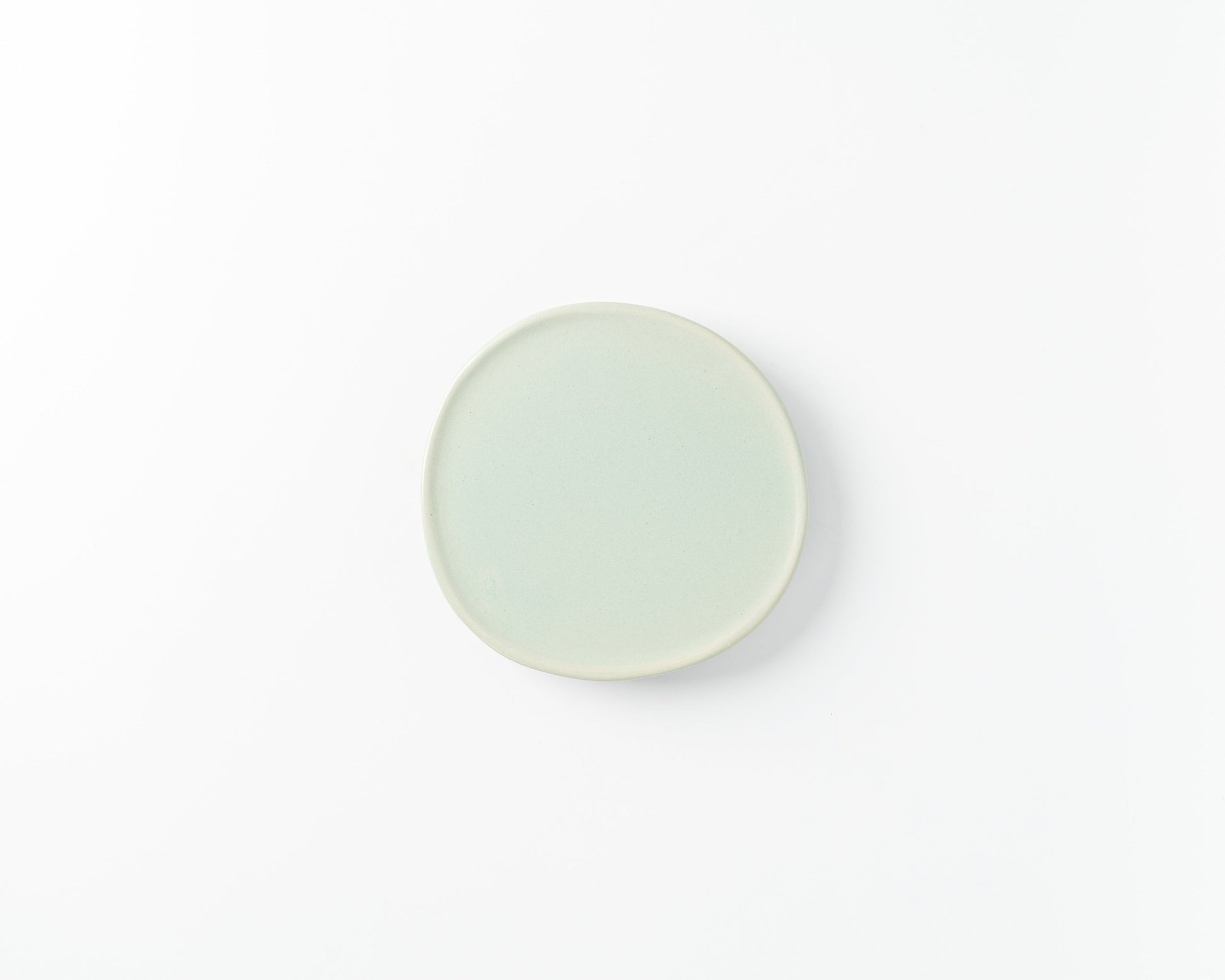 Minimalist round pale green ceramic plate on white background