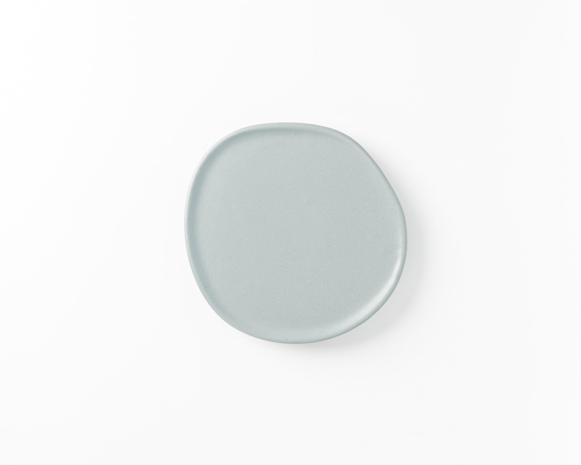 Minimalist round light gray ceramic plate with an irregular edge on white background