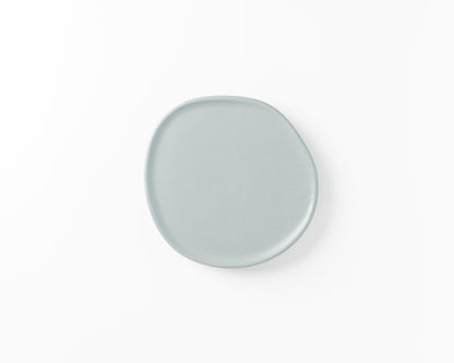 Minimalist round light gray ceramic plate with an irregular edge on white background