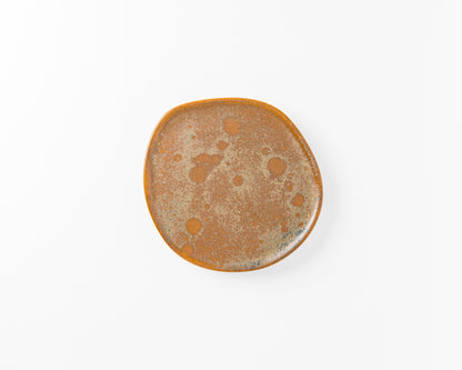 Round rustic ceramic plate with brown and speckled glaze on white background