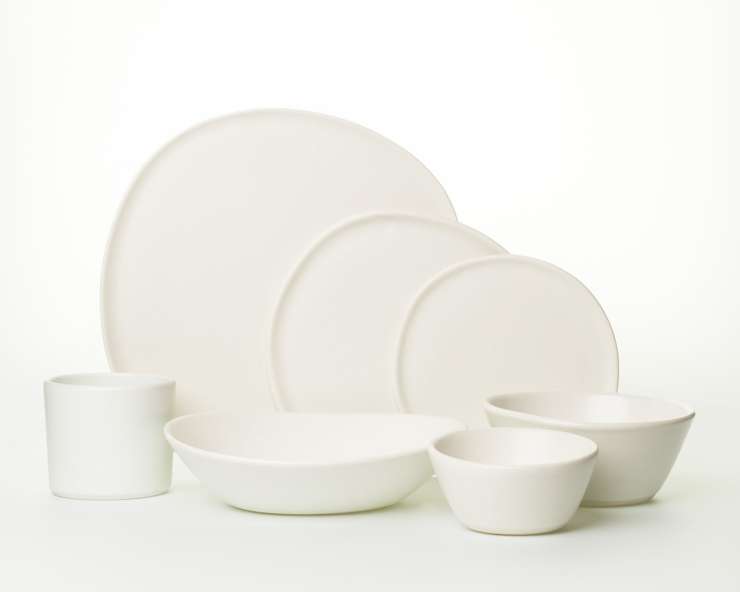 Set of minimalist white ceramic dinnerware including plates, bowls, and a cup on white background