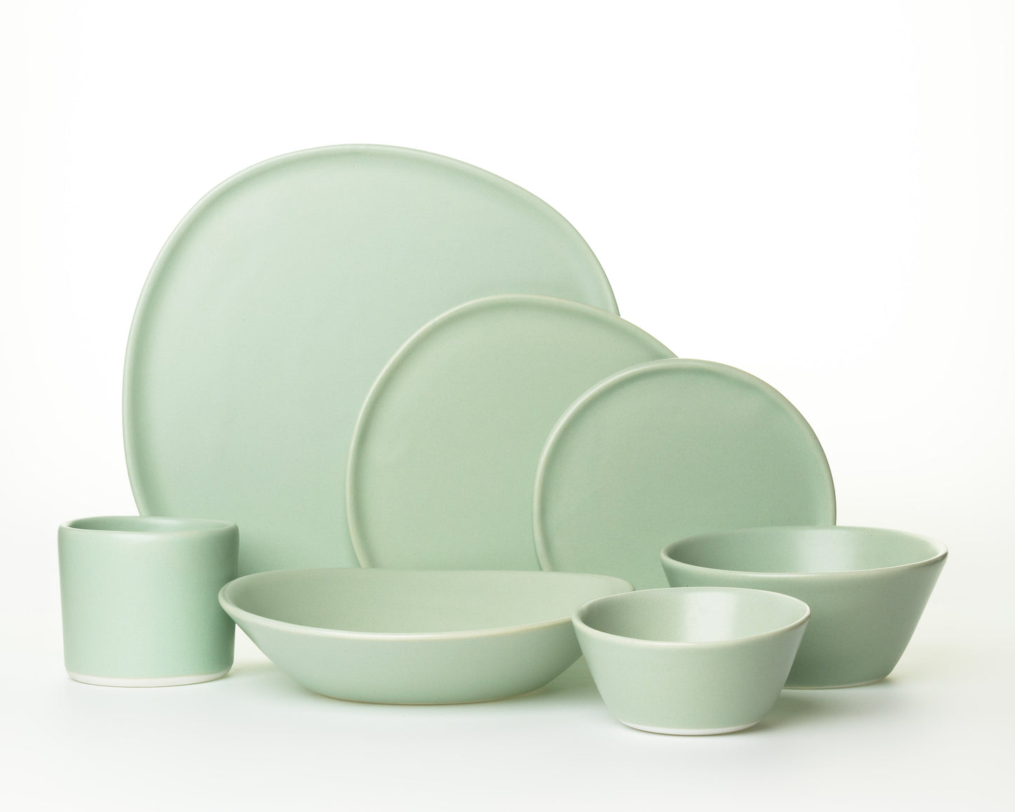 Set of matte light green ceramic dinnerware including plates, bowls, and a cup on white background