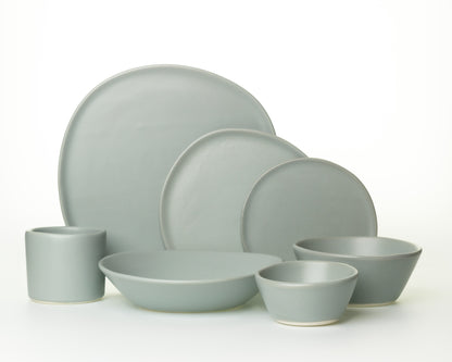 Set of seven matte gray ceramic dinnerware including plates, bowls, and a cup on white background
