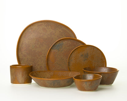 Rustic brown ceramic dinnerware set with plates, bowls, and mug on white background