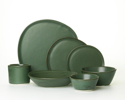 Green ceramic dinnerware set with plates, bowls, and a cup on white background