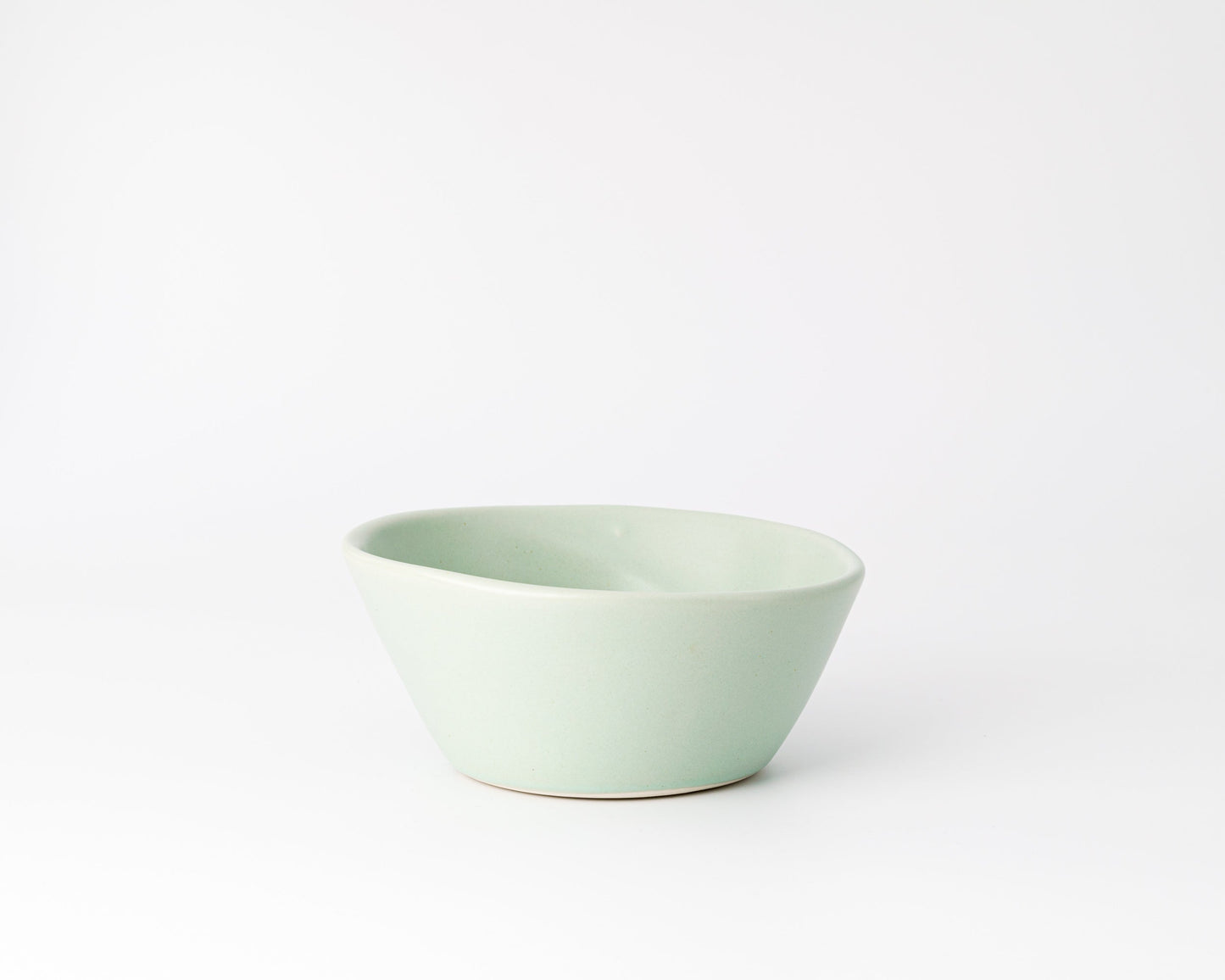 Light green ceramic bowl with an asymmetrical rim on a white background