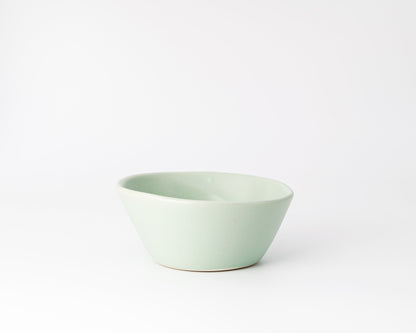 Light green ceramic bowl with an asymmetrical rim on a white background