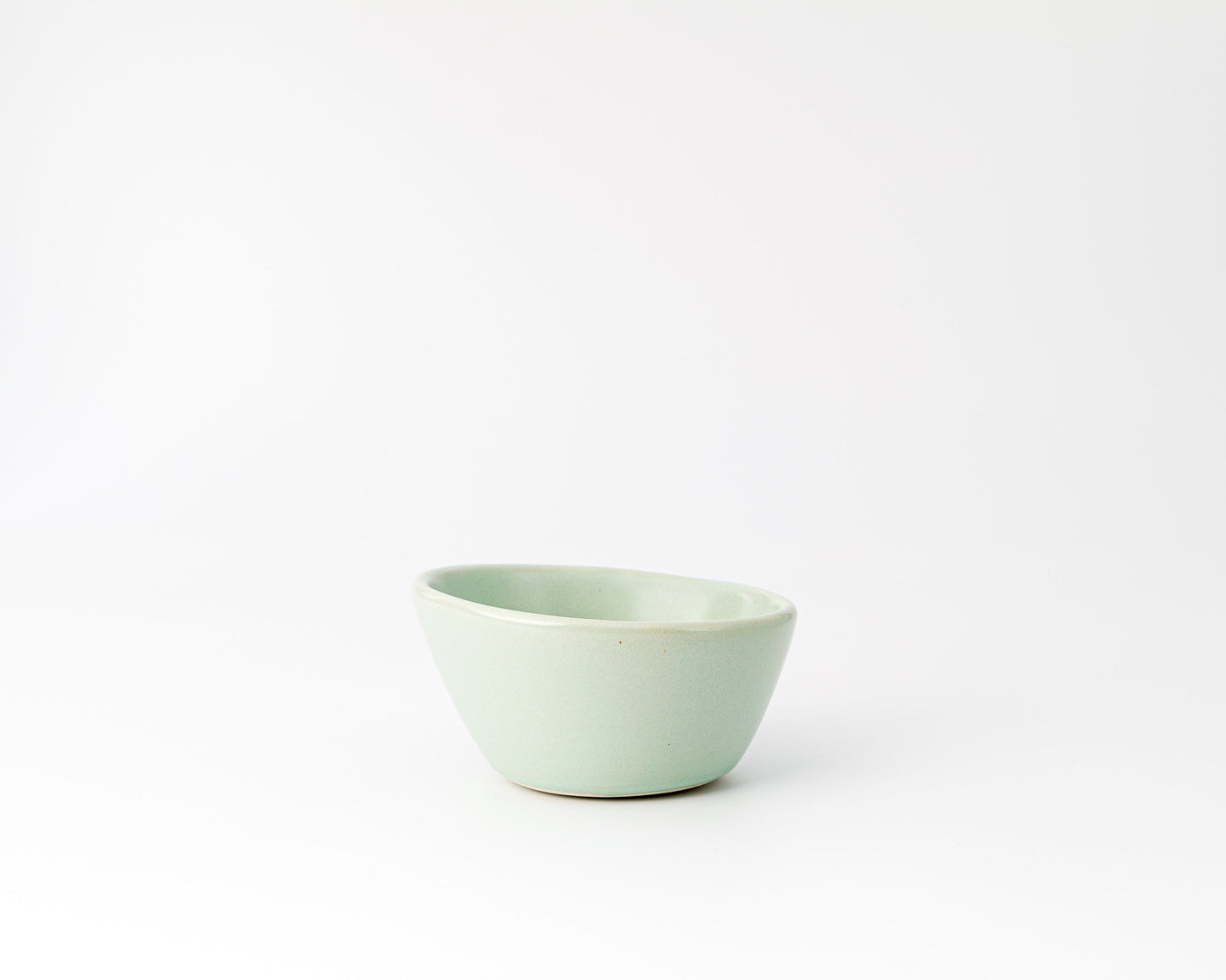 Small light green ceramic bowl with an asymmetrical rim on a white background