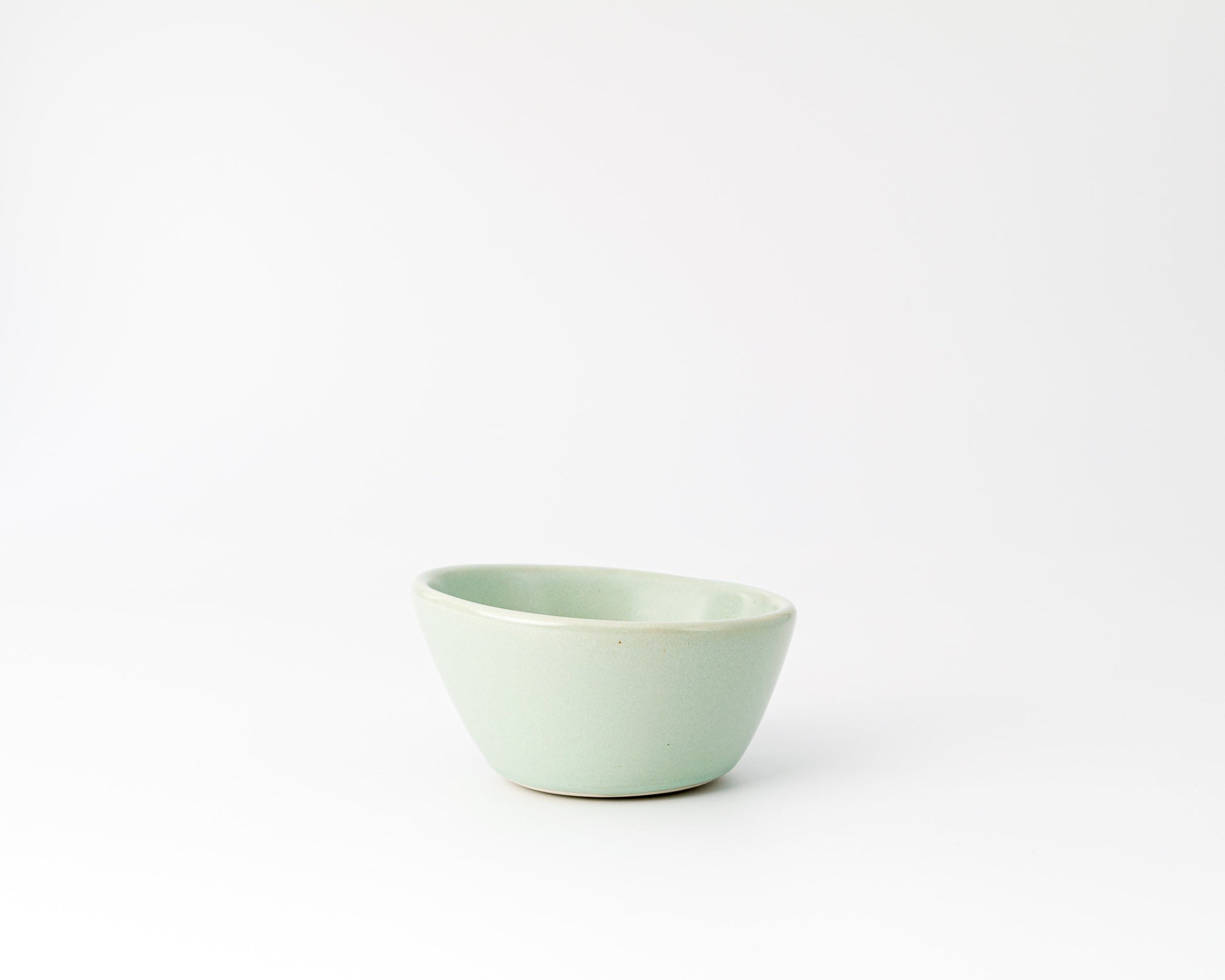 Small light green ceramic bowl with an asymmetrical rim on a white background