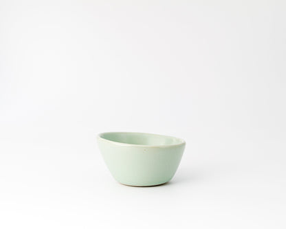 Small light green ceramic bowl with an asymmetrical rim on a white background
