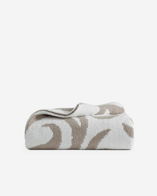 Taupe and off-white Casablanca patterned bed blanket folded neatly showing bold geometric swirl design on light gray background