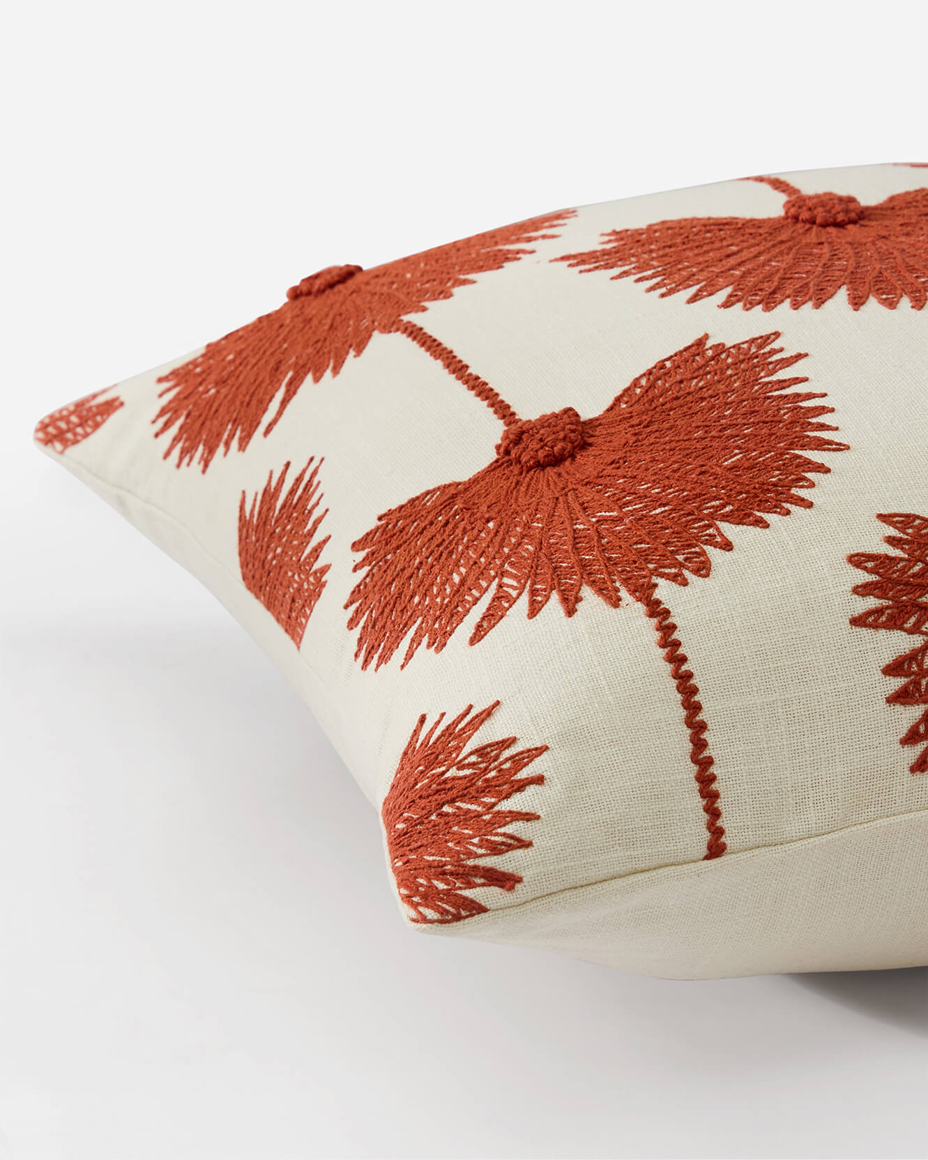 Angled corner detail of palm leaf embroidered throw pillow sienna off white variant showing raised sienna rust botanical embroidery stitch texture and linen weave on off white ground