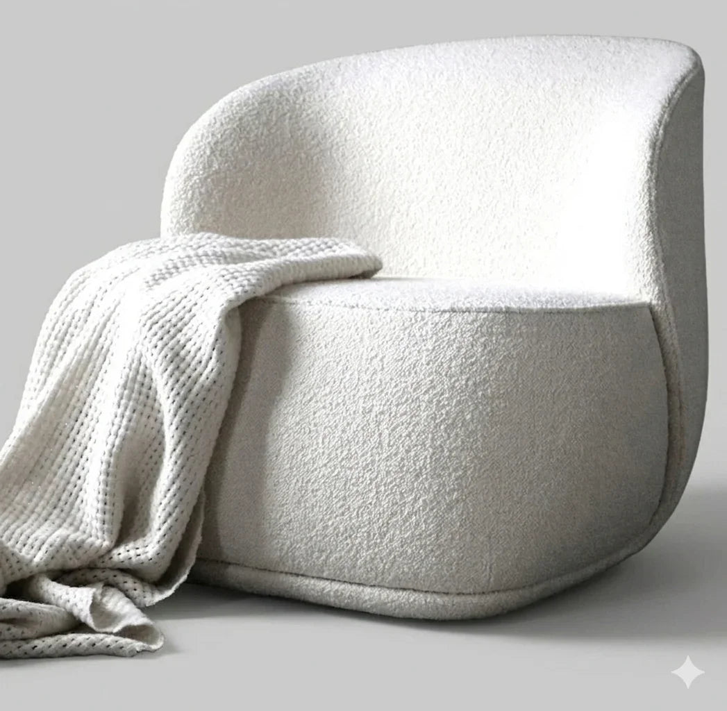 A lifestyle studio shot of the white boucle barrel chair with a soft knit throw blanket, presented on a light gray background to showcase comfort and texture.