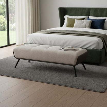 Beige tufted vegan leather bench with black splayed steel legs styled at the foot of a dark green upholstered bed on a gray area rug