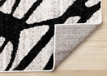 Black and gray abstract area rug folded back to show jute backing construction and serged edge finish on hardwood floor