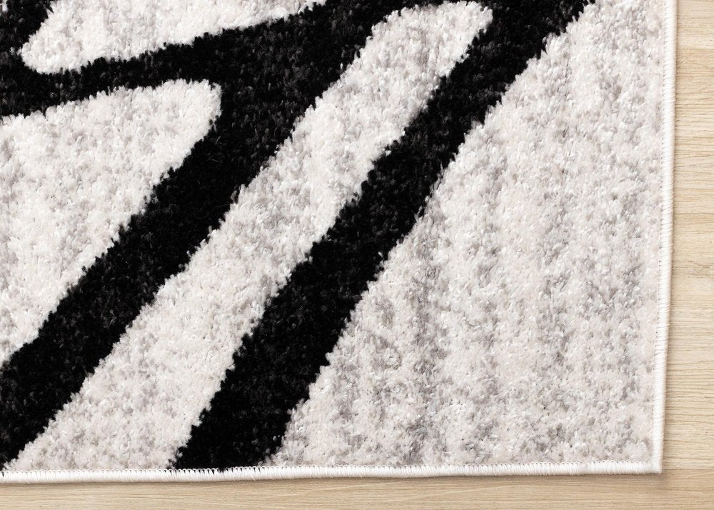 Black and gray abstract area rug corner detail showing dense polypropylene pile texture and serged edge finish on hardwood floor