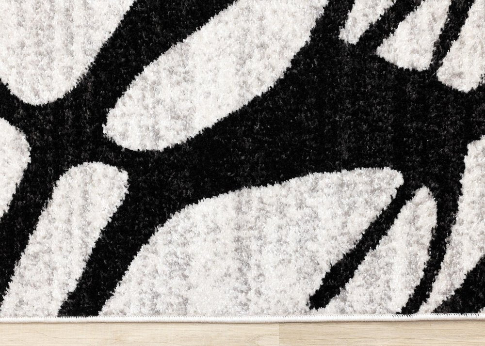 Black and gray abstract area rug low-angle edge view showing dense polypropylene pile depth and bold linear pattern contrast