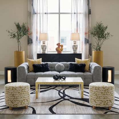 Black and gray abstract area rug styled in a modern living room with gray tufted sofa gold accents and sheer curtains