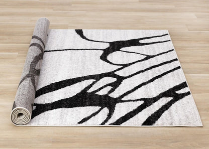 Black and gray abstract area rug partially rolled showing full linear pattern layout and jute backing on hardwood floor