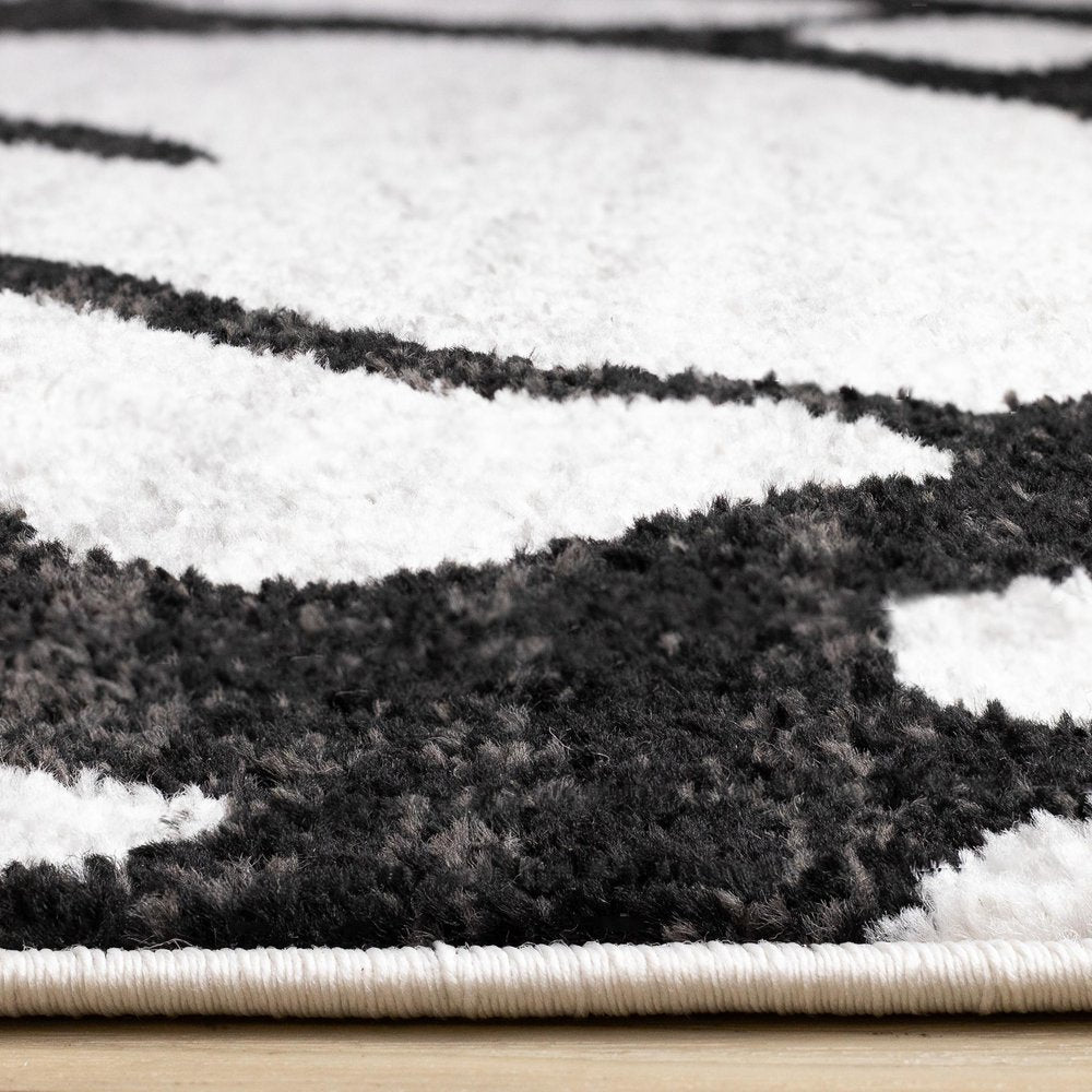 Black and gray abstract area rug side-angle view showing plush polypropylene pile depth and serged cream edge binding