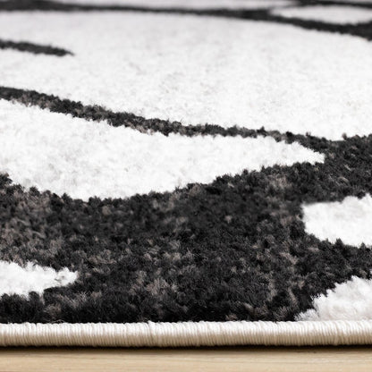 Black and gray abstract area rug side-angle view showing plush polypropylene pile depth and serged cream edge binding