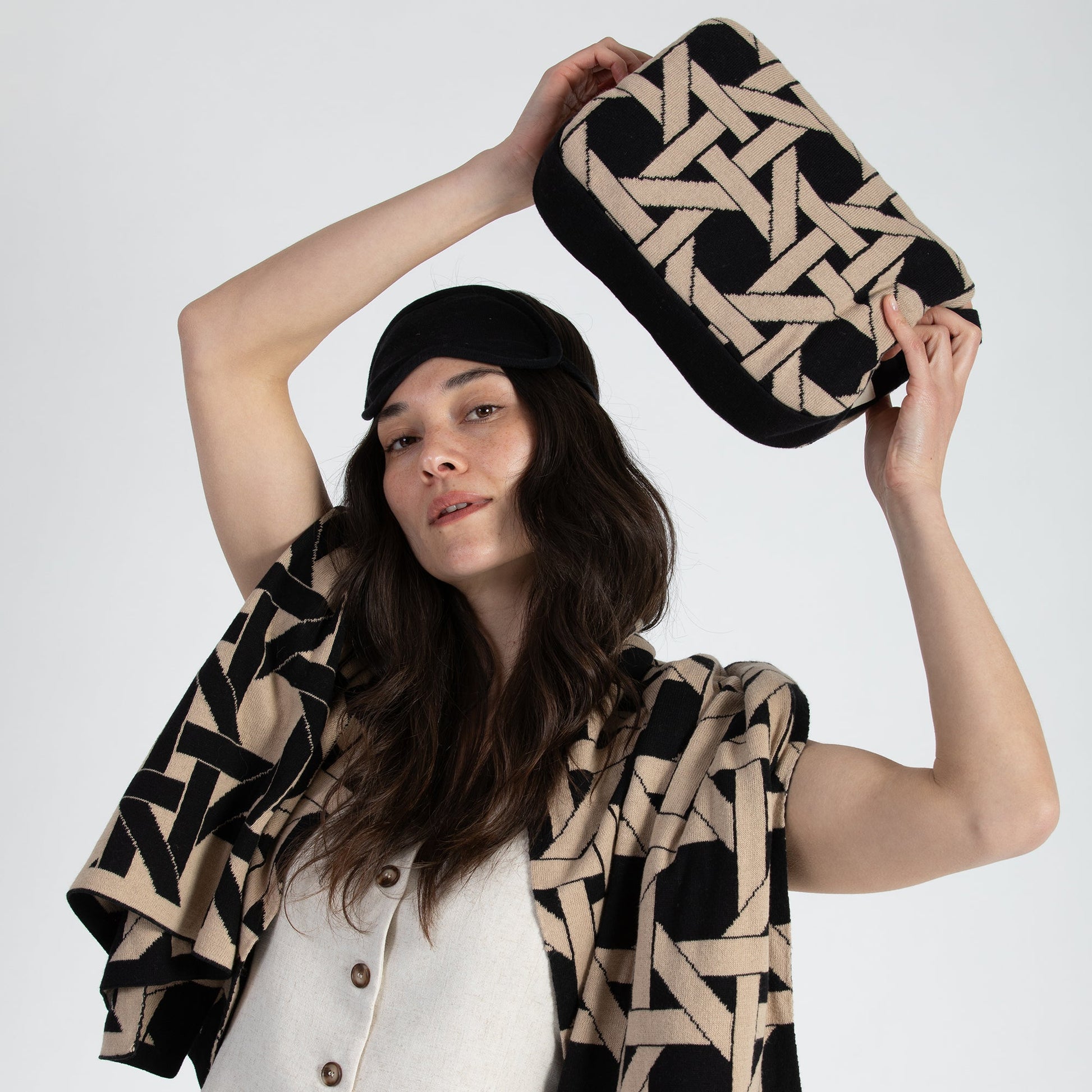 Woman holding black geometric organic cotton travel blanket compact pouch with matching blanket draped over shoulders