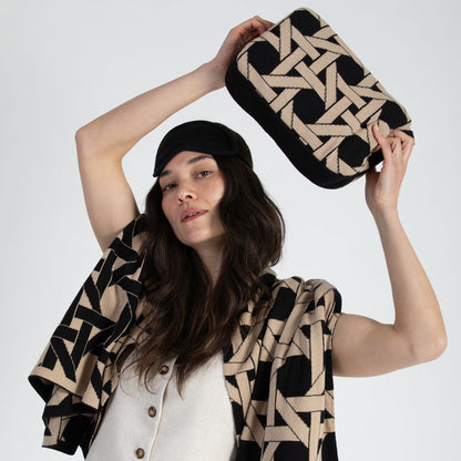Woman holding black geometric organic cotton travel blanket compact pouch with matching blanket draped over shoulders