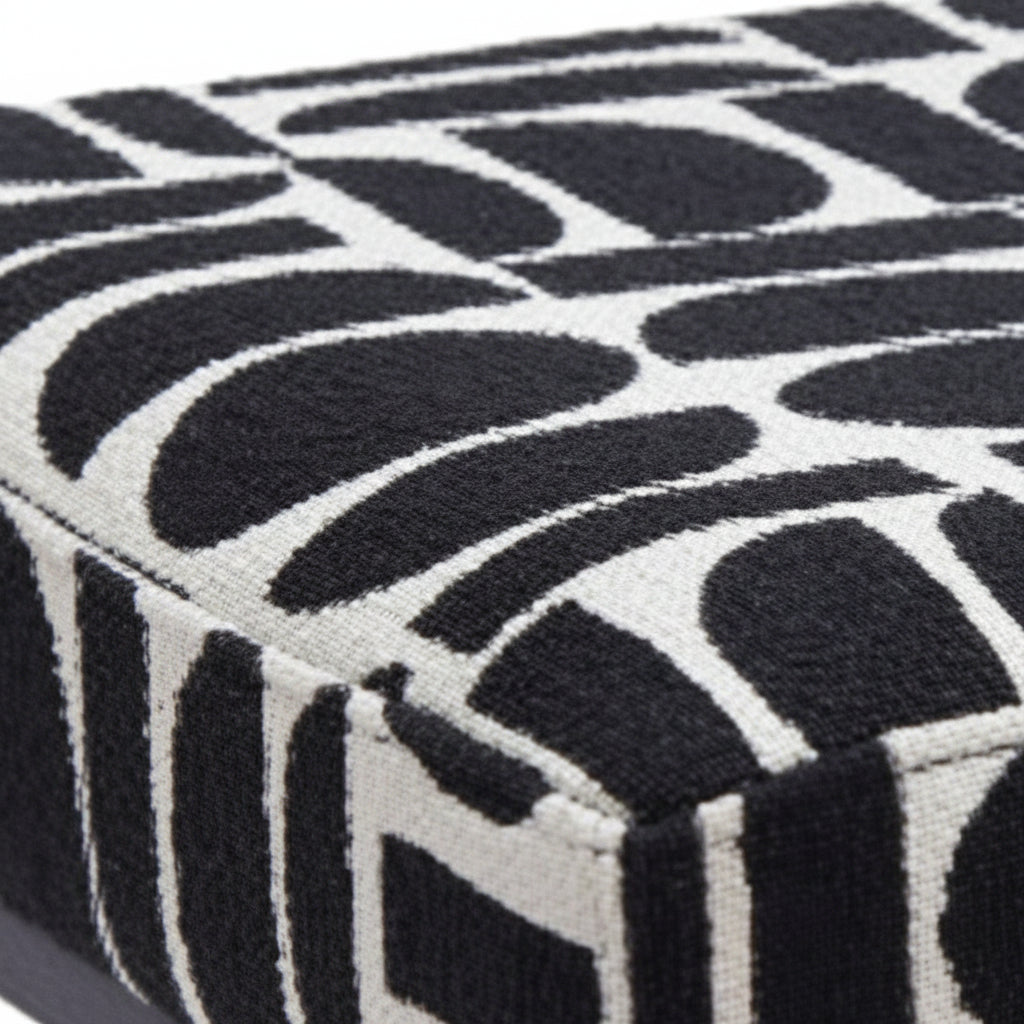 Angled close-up of black and white geometric polyester fabric bench seat corner showing texture and pattern detail with black pedestal leg base