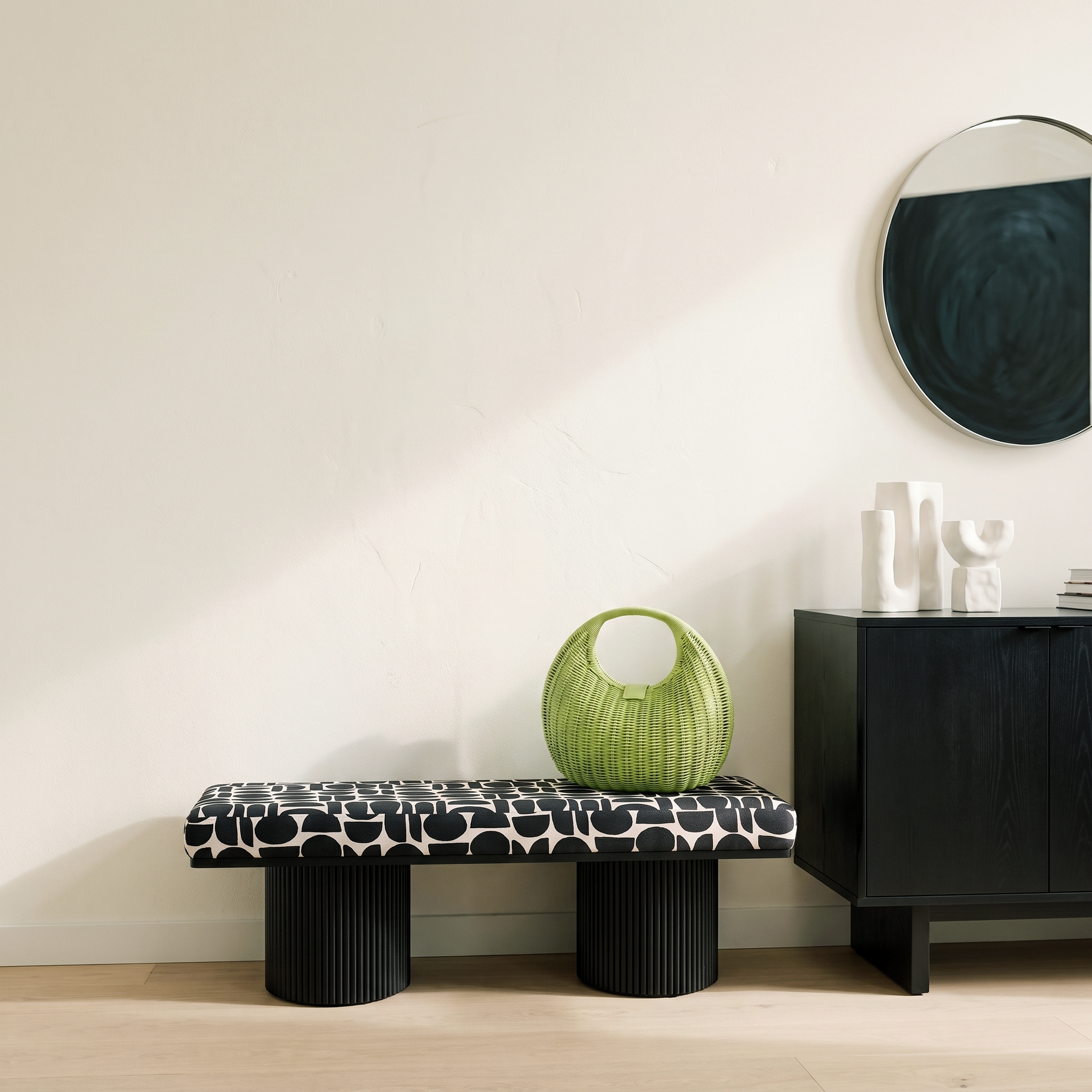 Black and white geometric patterned upholstered bench with ribbed black cylindrical pedestal legs styled against a cream wall with round mirror and black sideboard