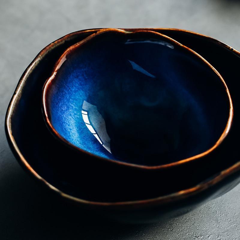 Detailed close-up of the Blue European Porcelain Dinnerware Set showing the rich textures of the dark blue glazed bowls with unique organic shapes and hand-painted metallic trim.