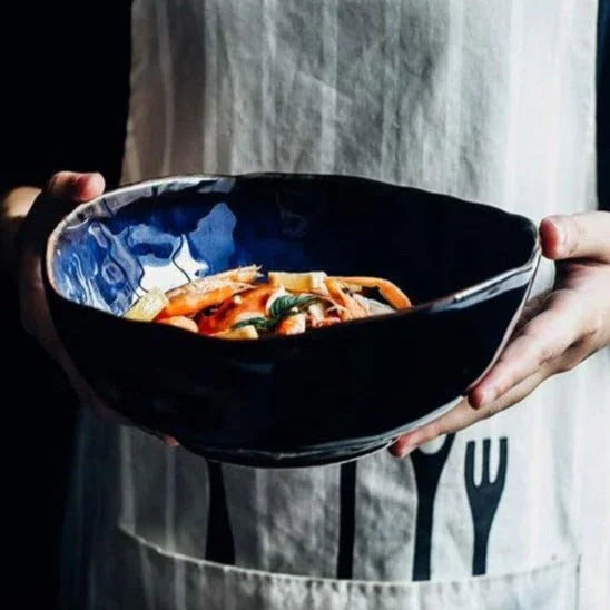 A person holding a large serving dish from the Blue European Porcelain Dinnerware Set, showcasing the artisanal dark blue glazed bowls and hand-painted porcelain texture.