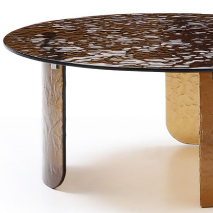 Close up of bronze tempered glass round coffee table showing rippled dark glass top surface and curved bronze leg texture detail on white background