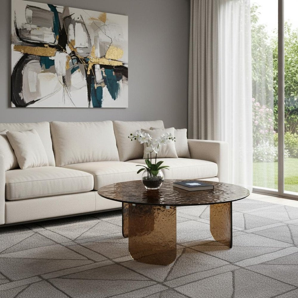 Bronze tempered glass round coffee table in a modern living room with ivory sofa, white orchid centerpiece, geometric area rug, and bold abstract art above