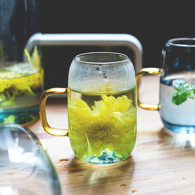 Clear glass cup with gold handle filled with yellow flower tea on wooden table