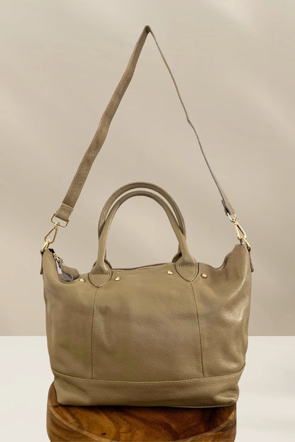 Neutral beige leather handbag with gold studs, dual handles, and detachable shoulder strap on wooden surface