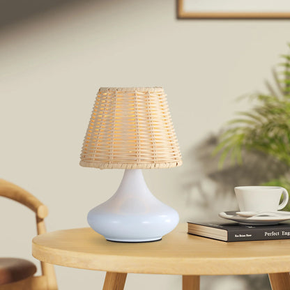 Table lamp with woven rattan shade and white ceramic base on round wooden table with book and cup