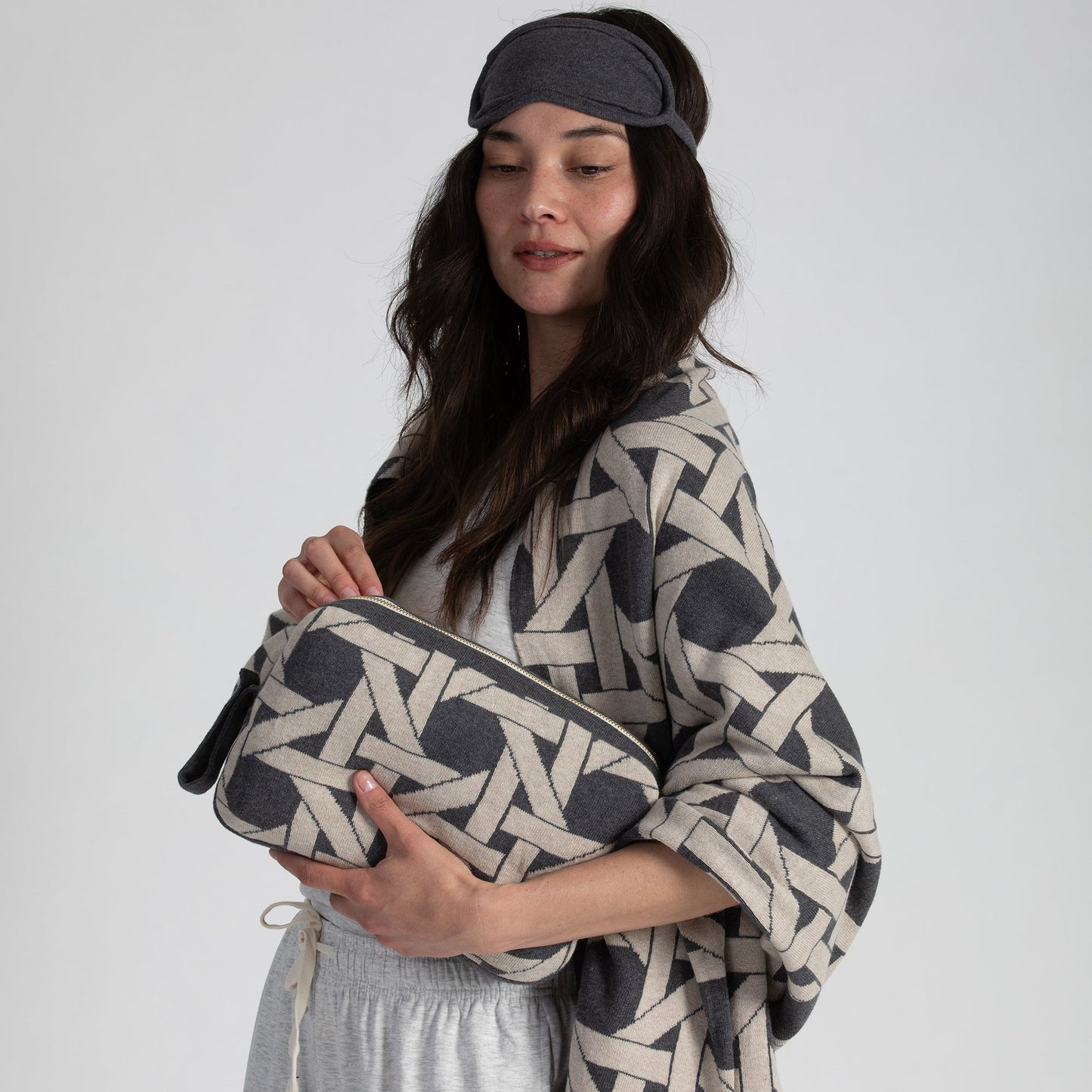 Woman wearing dark gray organic cotton travel blanket draped over shoulders with matching eye mask and geometric pouch