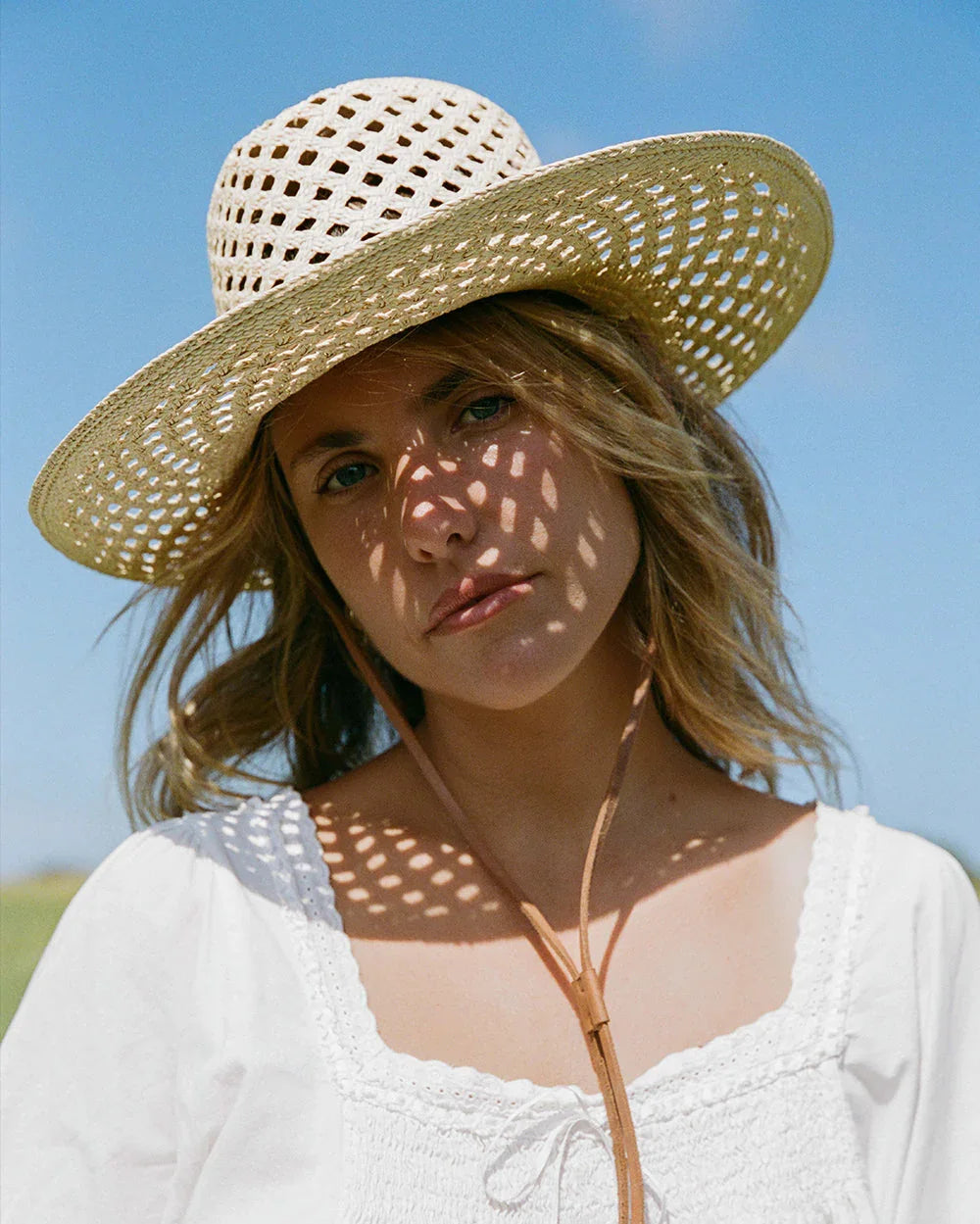 Woman wearing a white crochet sun hat and white blouse under clear blue sky