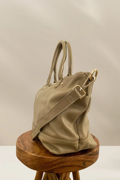 Beige pebbled leather handbag with gold hardware and detachable strap on wooden stool
