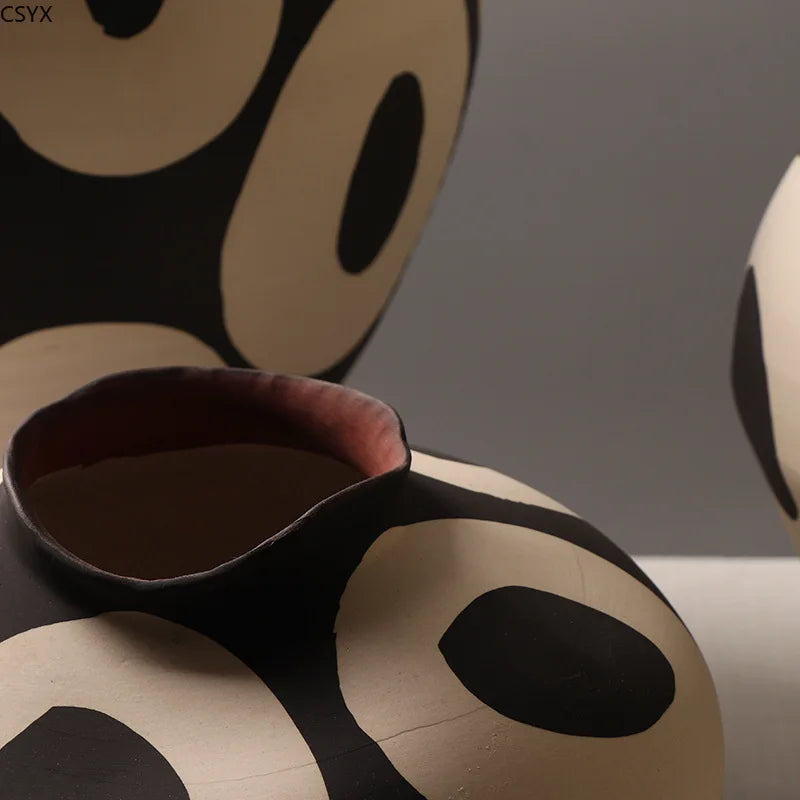 Close-up of an Aurelia geometric decorative vase showing its irregular curved rim, reddish-brown interior, and light circular patterns on a dark body.