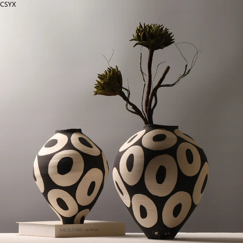 Two Aurelia geometric decorative vases with light circular patterns on dark rounded bodies, one displayed on a book and the other holding sculptural stems.