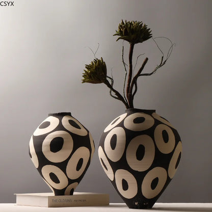 Two Aurelia geometric decorative vases with light circular patterns on dark rounded bodies, one displayed on a book and the other holding sculptural stems.