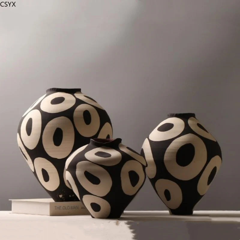 Three Aurelia geometric decorative vases with light circular patterns on dark rounded bodies, displayed in different sizes on a sunlit surface.