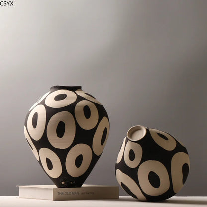 Two Aurelia geometric decorative vases with light circular patterns on dark bodies, one upright on a book and the other tilted to show its opening.